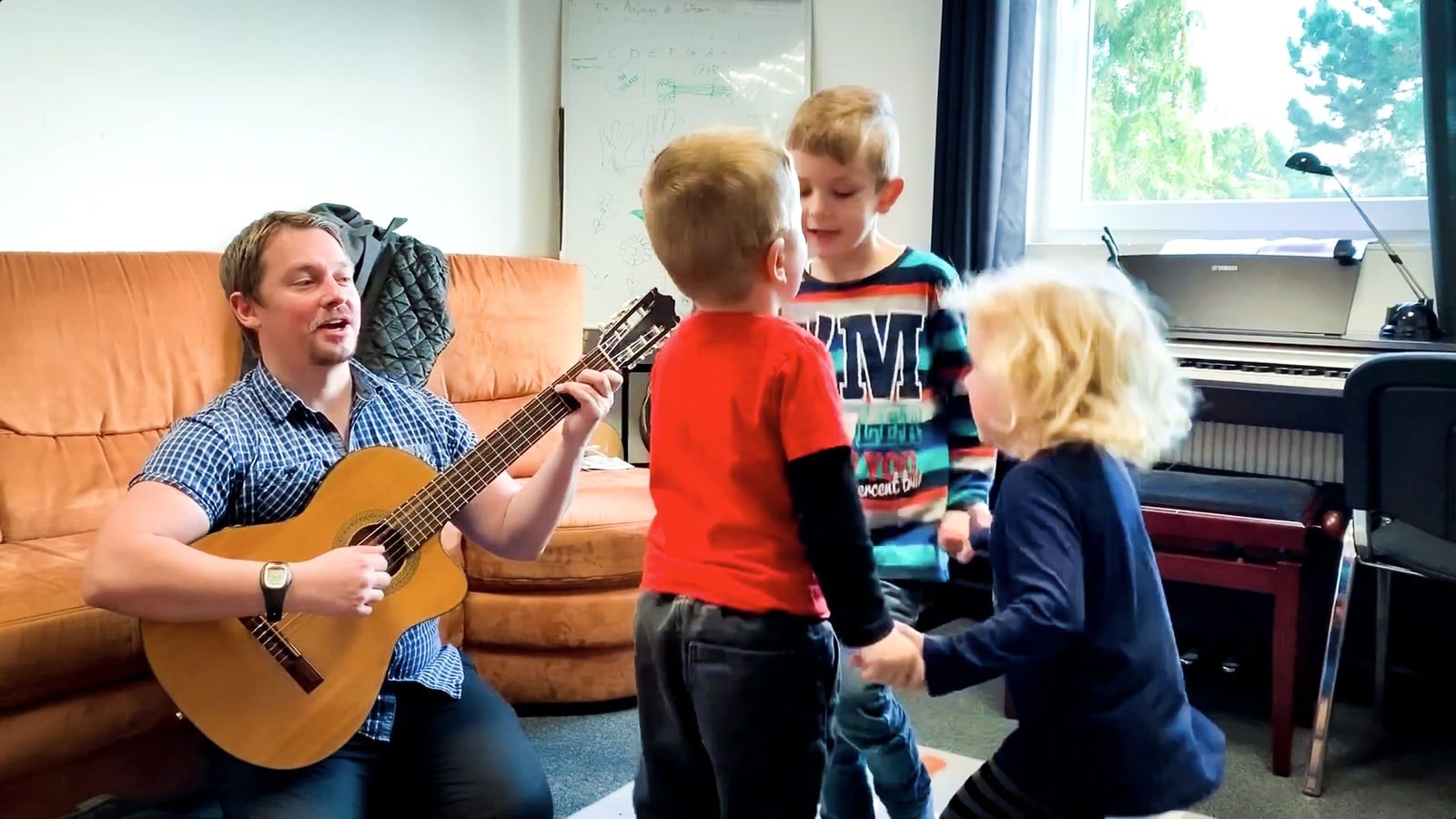 Lehrer mit Gitarre und drei kleine Kinder im Unterrichtsraum