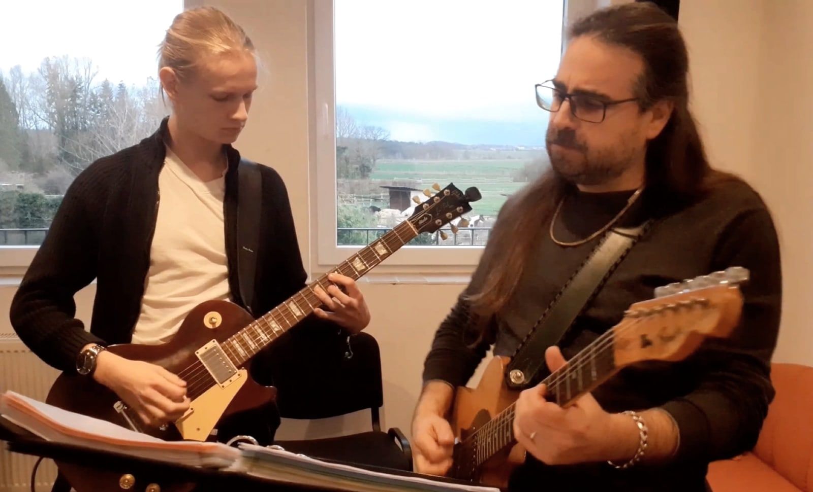 Jugendlicher und Lehrer mit E-Gitarren am Fenster